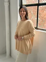 Sweater de punto color beige, de corte holgado y diseño asimétrico con tajos laterales. Presenta cuello redondo y mangas largas con puños acanalados, además de un detalle de costura vertical central.