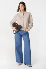 Saco tipo cardigan de punto color crudo, con cuello redondo, cierre frontal de botones y mangas largas con puños acanalados.