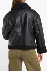 Campera tipo gamulán de cuero sintético negro con interior y detalles de cuello y puños en corderito negro. Presenta cierre frontal y diseño oversize.