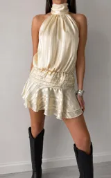 Vestido corto de satén color crema con diseño de rayas verticales sutiles. Presenta cuello alto tipo halter, cintura elástica fruncida y falda con volados en el ruedo.