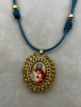 Collar ajustable con cordón azul y dije central ovalado con imagen religiosa, rodeado por una estructura de cuentas multicolores.