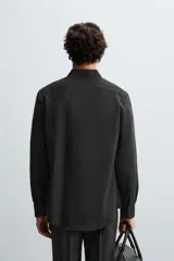 Camisa negra de corte slim fit, con cuello italiano y manga larga con puño abotonado. Cierre frontal de botonadura.
