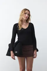 Top de tejido acanalado negro, con escote en V, mangas largas con terminación acampanada y ajuste al cuerpo.
