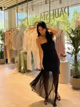 Vestido midi negro con escote palabra de honor, cuerpo entallado y falda con sobrecapa de tul transparente que aporta volumen y movimiento.