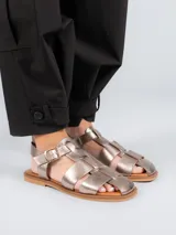 Sandalias tipo pescador con diseño de tiras anchas entrelazadas, confeccionadas en cuero color plateado. Presentan cierre mediante hebilla metálica lateral, plantilla de cuero y suela plana de goma.