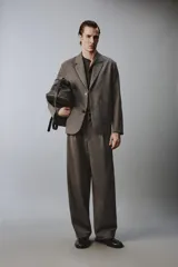 Pantalón de traje wide fit color marrón oscuro con textura, pinzas frontales, bolsillos laterales y cierre con cremallera y botón.