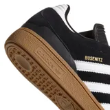 Championes Adidas Busenitz Pro, modelo de skate en color negro con las icónicas tres tiras blancas laterales y suela de goma color caramelo. Presenta una lengüeta larga característica y detalles en dorado.