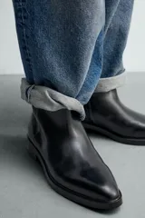 Bota de cuero negro con diseño minimalista, punta fina, cierre lateral con cremallera y tacón bajo.