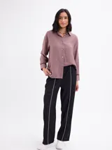 Camisa de manga larga color malva, con cuello clásico, cierre frontal con botones y detalles de vivos negros en los puños.