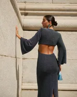 Vestido largo color verde esmeralda, con escote en V, corte a la cintura y falda con abertura lateral. Mangas largas acampanadas y espalda descubierta.