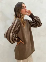 Sweater de lana color crudo con mangas largas abullonadas en gris y blanco, con diseño de rayas y perforaciones. Cuello redondo y puños acanalados.