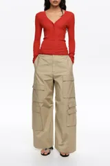 Pantalón cargo beige de tiro bajo y corte ancho, con múltiples bolsillos con solapa en los laterales de las piernas y cierre frontal con botón y cremallera oculta.