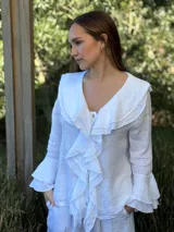 Camisa de lino azul marino con volados en cascada a lo largo del frente y en los puños de las mangas largas. Presenta un escote en V con un botón de nácar visible.