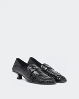 Mocasines de cuero vacuno negro con acabado naplak de efecto arrugado, tacón fino bajo de 3 cm y detalle de placa metálica con la inicial D en la tira frontal.