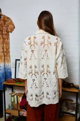 Camisa holgada color crema con bordados de palmeras y frutos, confeccionada en algodón. Presenta terminación de puntilla en el ruedo.