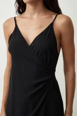 Vestido negro midi de tirantes finos, con escote cruzado en V y diseño envolvente con drapeado lateral que genera una abertura frontal.