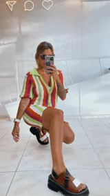 Vestido corto tejido calado a rayas horizontales en tonos naranja, amarillo y blanco, con cuello tipo polo y cierre frontal con botones.