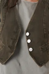 Chaleco de gabardina color blanco, con escote en V, cierre frontal con botones y bolsillos delanteros simulados.