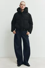 Campera puffer acolchada de color negro, con cuello envolvente, capucha integrada, manga larga, bolsillos laterales ocultos y bajo con elástico. Cierre frontal con botones a presión ocultos por solapa.
