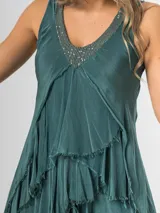 Vestido largo negro de seda italiana con diseño sin mangas de bretel ancho y escote en V profundo con detalles de paillettes plateados. Presenta múltiples capas con volados y bordes deshilachados que aportan movimiento y una caída fluida.