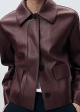 Chaqueta de cuero sintético marrón con cuello camisero, cierre frontal con botones oscuros y bolsillos frontales con solapa.