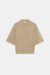 Polo de corte holgado confeccionado en mezcla de lyocell, con cuello solapa, cierre frontal de botones y mangas cortas amplias.