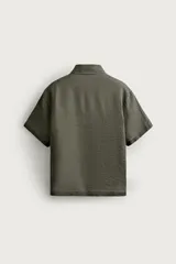 Camisa regular fit confeccionada en tejido de lino, color blanco, con cuello solapa, manga corta y cierre frontal de botonadura.