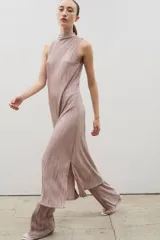 Vestido midi de diseño plisado en color rosado, con cuello alto y sin mangas. Presenta un tajo lateral y corte holgado, diseñado para ser usado en conjunto con pantalones del mismo tejido.