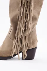 Bota bucanera de caña alta confeccionada en cuero vacuno, con diseño de estilo western que presenta flecos laterales largos y taco cuadrado.