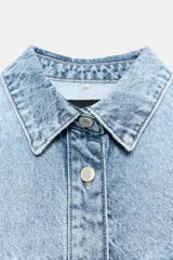 Cazadora de denim oversize con capucha gris desmontable, cuello camisero, cierre frontal con botones metálicos y bolsillos delanteros de plastrón.