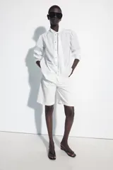 Camisa de algodón color blanco, con cuello subido y detalle de pañuelo incorporado, manga larga con puños anchos y cierre frontal con botones joya dorados.