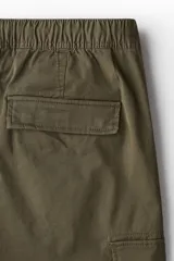Pantalón cargo de corte ajustado en tejido de algodón, con cintura elástica y cordón de ajuste. Presenta bolsillos laterales tipo cargo con solapa, bolsillos al bies y bolsillos traseros. Incluye costuras reforzadas y pinzas en las rodillas para mayor movilidad.