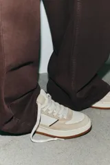 Zapatillas deportivas de cuero color beige y blanco, con suela marrón de goma y cierre con cordones.