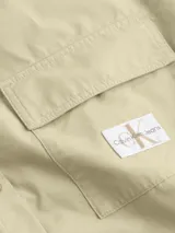 Camisa de estilo utility con corte oversized y largo, confeccionada en algodón. Presenta cuello en punta, cierre frontal de botones, bolsillo de parche en el pecho con insignia de la marca y bajo redondeado.