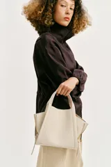 Bolso bandolera de formato city color marrón, con diseño estructurado, pespuntes decorativos, doble asa de mano y cremalleras laterales con tiradores colgantes.