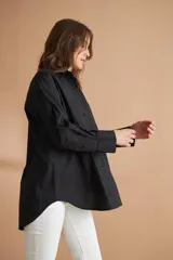 Camisa negra de corte holgado con cuello clásico, cierre frontal con botones, manga larga con puños abotonados y bolsillo de parche en el pecho.
