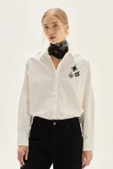 Camisa blanca de corte oversize, confeccionada en algodón, con cuello clásico y cierre frontal de botones. Presenta un bordado de corazones en el pecho.