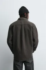 Sobrecamisa de corte relajado confeccionada en tejido de algodón con textura. Presenta cuello solapa, cierre frontal con botones, manga larga con puños abotonados y un bolsillo plastrón en el pecho.