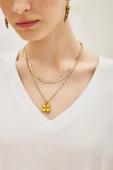 Collar doble en tono dorado, compuesto por una cadena tipo serpiente y una cadena fina con dije de trébol de cuatro hojas en acrílico amarillo con un pequeño cristal central.