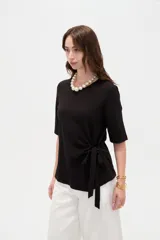 Remera negra de manga corta, con cuello redondo y diseño holgado con detalle de lazo para anudar en la cintura.