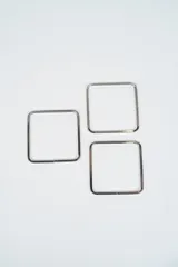 Set de tres brazaletes rígidos de forma cuadrada, fabricados en metal plateado con acabado brillante.