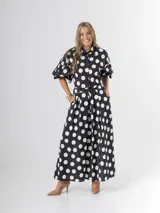 Conjunto de dos piezas con estampa polka dots en negro y blanco, compuesto por un pantalón tipo culotte de tiro alto con bolsillos y una blusa estilo camisa con mangas globo y cierre frontal de botones.