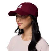 Gorro unisex de algodón color bordó, con visera curva y cierre de velcro ajustable en la parte trasera. Presenta un parche frontal con el logo de Columbia Sportswear y un oso.