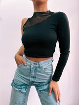 Top corto negro con una manga larga y cuello alto. Presenta un diseño asimétrico con un panel de tul transparente que cubre el hombro y parte del pecho.