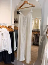 Vestido maxi de lino color crudo, con escote en V, tiras finas regulables y detalles de flecos frontales.