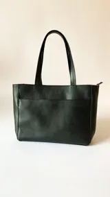 Cartera tipo tote de cuero graneado negro, con diseño clásico y textura uniforme. Cuenta con doble asa de hombro, bolsillo frontal con cierre magnético, bolsillo trasero con cierre metálico y compartimento principal con cierre. El interior está forrado y dispone de múltiples bolsillos organizadores.