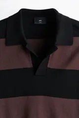 Remera polo de punto con diseño a rayas horizontales en color negro y marrón, de manga corta, cuello camisero con abertura en V y corte holgado.