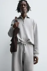 Polo de punto de corte relajado, confeccionado en mezcla de algodón, con cuello solapa, cierre frontal de cremallera y manga larga con acabados en rib.