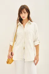 Campera de gabardina color crudo con cuello camisero, mangas largas regulables con tira y botón, y cierre frontal con botones ocultos. Presenta parches bordados decorativos en el delantero y la espalda, además de bolsillos laterales tipo ojal.
