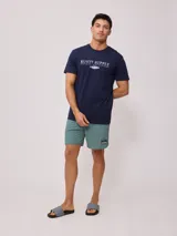 Short de baño tipo volley color verde azulado, con cintura elástica y cordón de ajuste en color azul marino. Presenta un parche con el logo de la marca en la pierna izquierda y aberturas laterales en el ruedo.